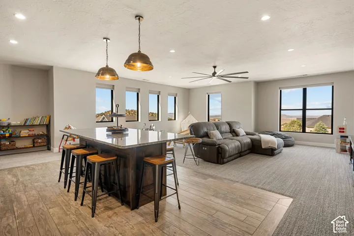 Spacious open-concept living area featuring wood-finish flooring, a large kitchen island with a light-toned countertop, multiple windows, and recessed lighting