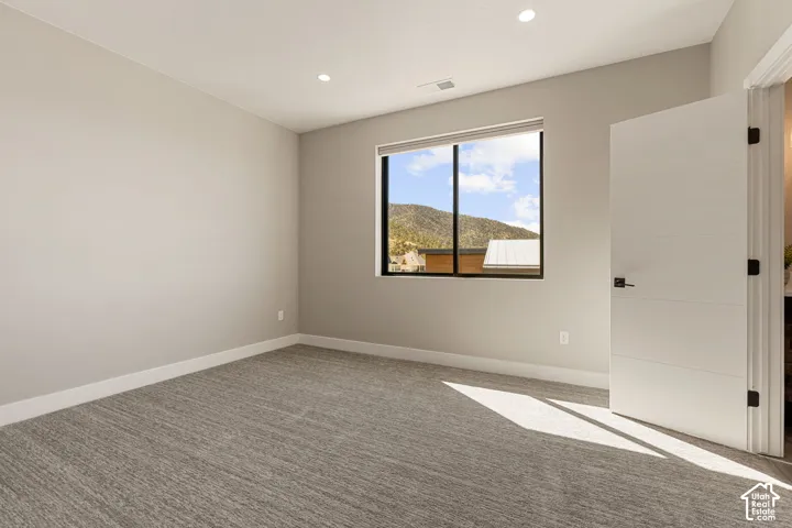 Recessed ceiling lighting, textured gray carpeting, window with black framing, white interior door with dark hardware, and light neutral wall finishes