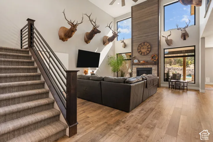 Two-story living area featuring a stone and wood-paneled fireplace, wood-finish flooring, and large windows