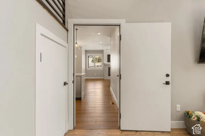 Wood-finish flooring, white doors with matte black hardware, and an open doorway leading to a brightly lit room