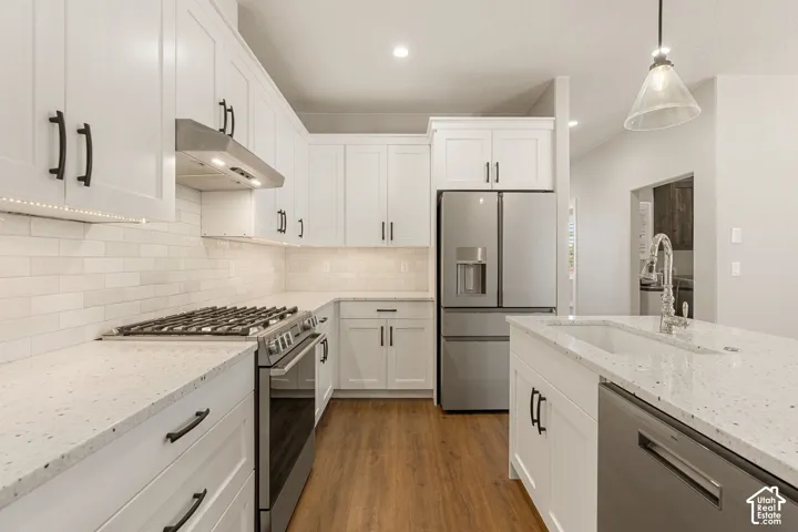 White shaker cabinetry with black hardware, stainless steel appliances, speckled countertops, white subway tile backsplash, and wood-finish flooring