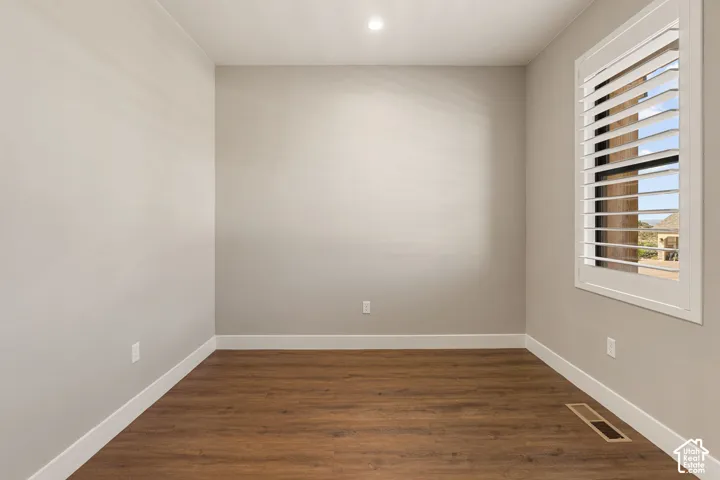 Wood-finish flooring with white trim, a recessed ceiling light, and a window featuring white plantation shutters