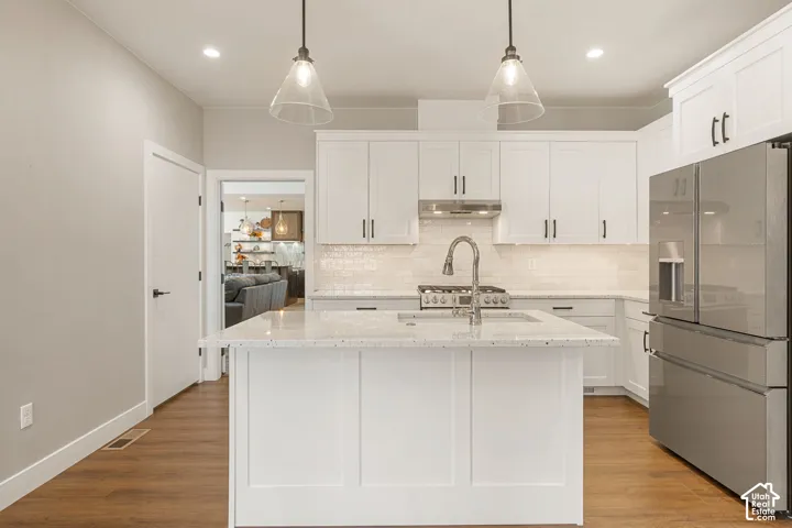 Kitchen featuring a central island with a solid surface countertop, white cabinetry with dark hardware, stainless steel appliances, wood-finish flooring, and pendant lighting