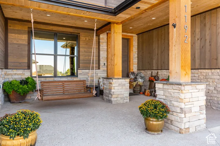 Covered patio with stone and wood-finish siding, exposed wood ceiling, a large window, and a wood porch swing