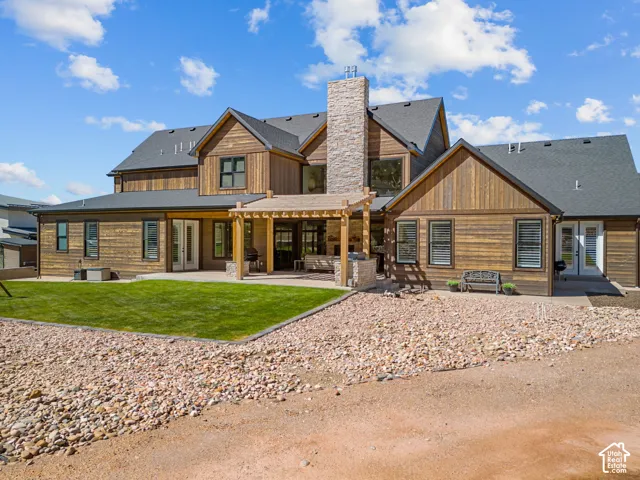Wood siding exterior with a dark shingle roof, stone chimney, and a covered patio with a wood pergola