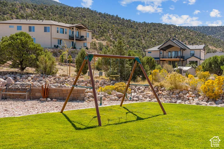 Expansive lawn with a swing set, bordered by a decorative rock wall and natural landscaping