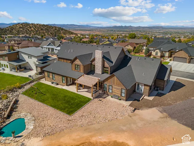 Expansive property featuring a multi-level wood-clad exterior, a stone-clad chimney, a covered patio with a pergola, a manicured lawn area, and a rock-lined pond