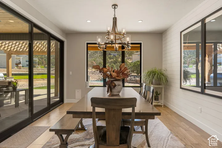 Spacious dining area featuring wood-finish flooring, a contemporary chandelier, recessed lighting, and expansive sliding glass doors leading to an outdoor patio with a pergola