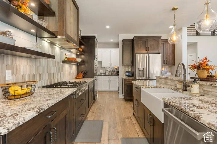 Gourmet kitchen featuring wood-finish flooring, custom cabinetry, full-height decorative tile backsplash, built-in stainless steel appliances, and dual pendant lighting