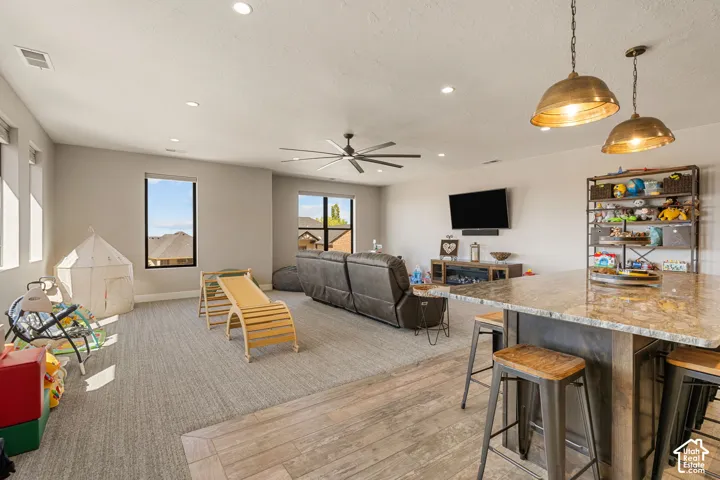Recessed lighting, ceiling fan, wood-finish flooring, island with a stone countertop, and pendant lighting