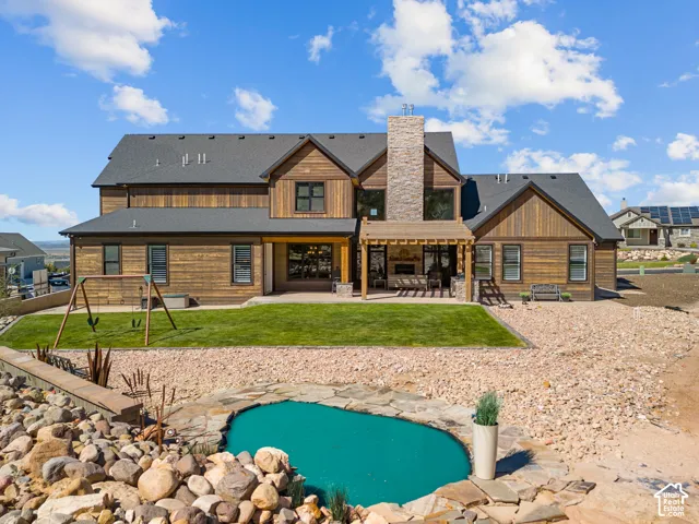 Wood-finish siding with a stone chimney, expansive back patio with a pergola, and a built-in outdoor fireplace