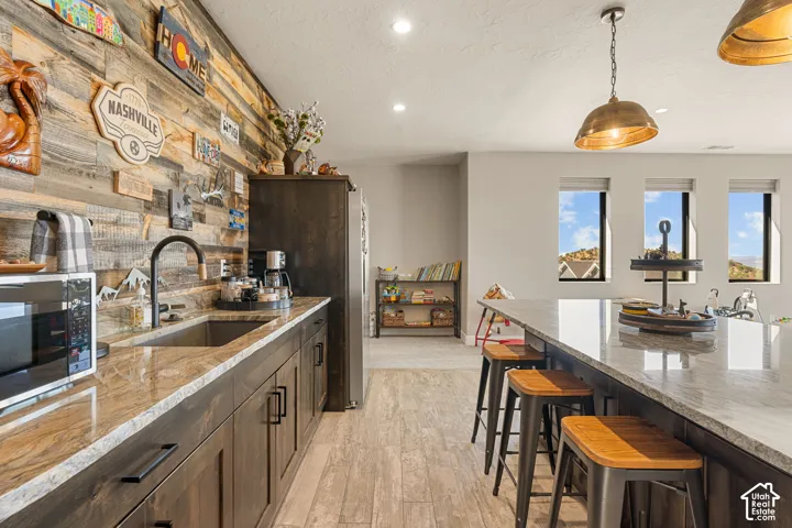 Kitchenette featuring wood-finish flooring, dark wood-finish cabinetry, light-toned countertops, and a stainless steel sink with a black-finish faucet