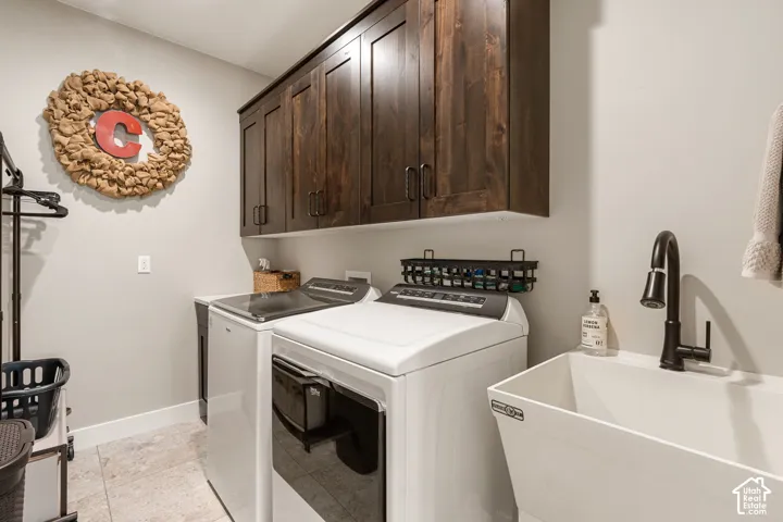 Laundry area featuring wood-finish cabinetry, a utility sink with a black faucet, and light tile flooring