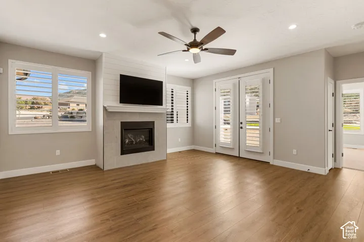 Living area featuring wood-finish flooring, a contemporary fireplace with a shiplap accent wall, white plantation shutters, and French doors