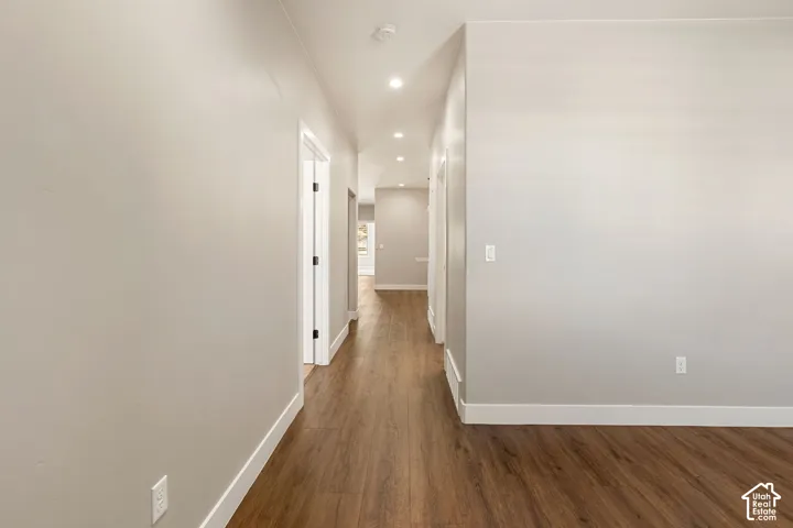Hallway featuring wood-finish flooring, recessed lighting, white baseboards, and neutral wall tones