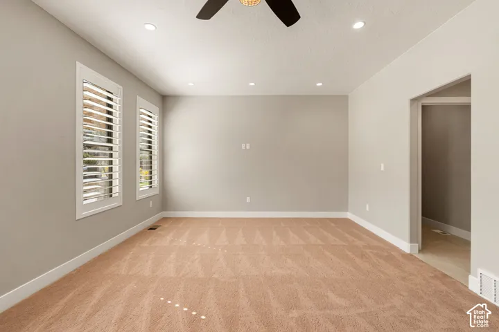 Recessed ceiling lighting, a ceiling fan, dual windows with plantation shutters, neutral-toned walls, and plush carpeting