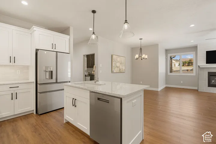 Kitchen featuring white cabinetry, stainless steel appliances, a white subway tile backsplash, and a central island with a sink and pendant lighting
