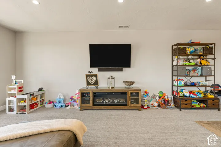 Recessed lighting, wall-mounted television, built-in media console with fireplace, and a large carpeted area