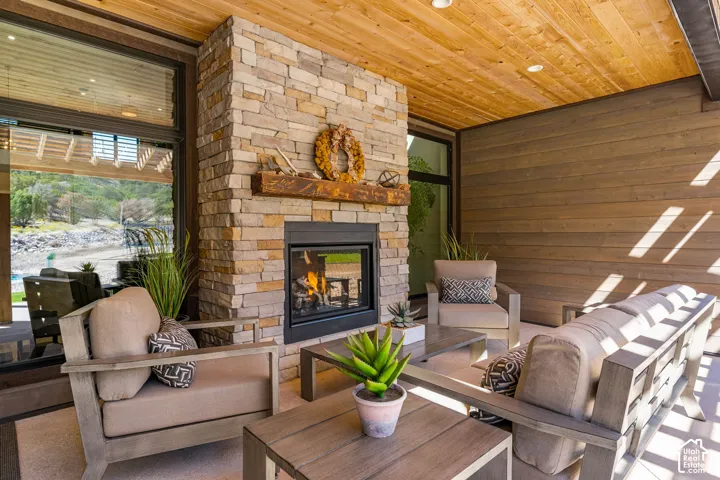Covered patio featuring a stone-clad fireplace with a wood mantle, wood-paneled ceiling, and wood-finish wall siding