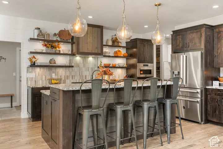 Kitchen with dark wood-finish cabinetry, stainless steel appliances, a multi-level island with a light-toned countertop, and wood-finish flooring