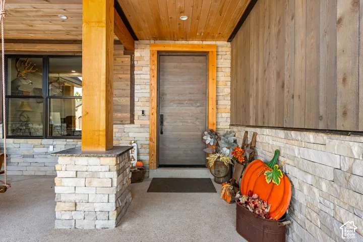 Wood-paneled ceiling, stone veneer siding, wood-finish door, large wood support beam, and black-framed windows