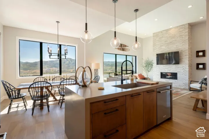 Open-concept living area featuring wood-finish flooring, a contemporary fireplace with a stone-clad surround, and a kitchen island with integrated sink
