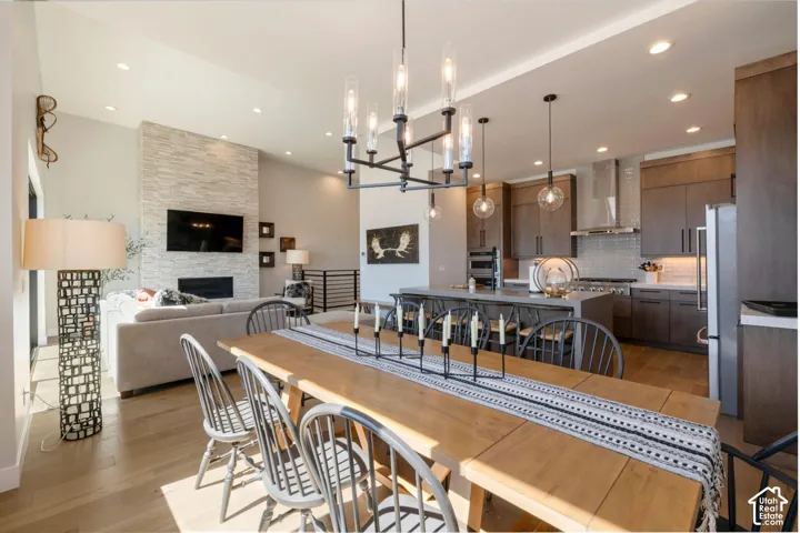 Open-concept living space featuring wood-finish flooring, a stacked stone fireplace, a kitchen with dark wood-finish cabinetry, and a large central island with seating