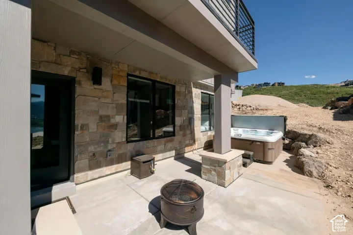Stone veneer exterior with a concrete patio, integrated hot tub, and a fire pit