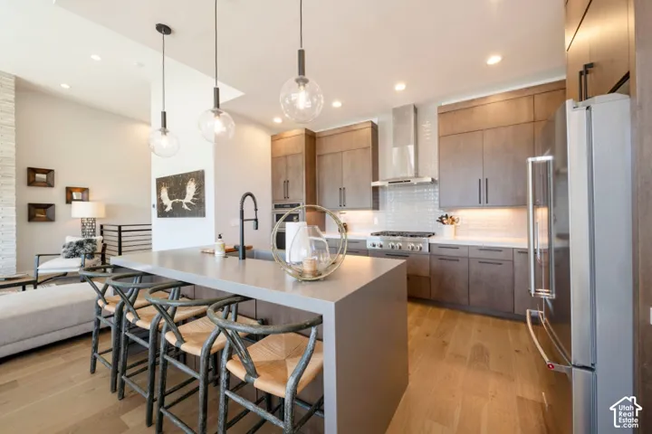 Open-concept kitchen with a large island, wood-finish flooring, stainless steel appliances, and pendant lighting