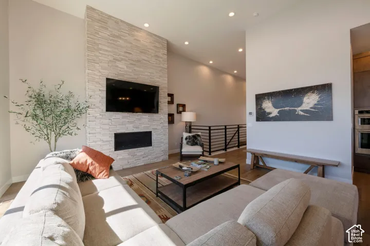 Vaulted ceiling, recessed lighting, floor-to-ceiling stone-clad fireplace, built-in linear fireplace, and wood-finish flooring