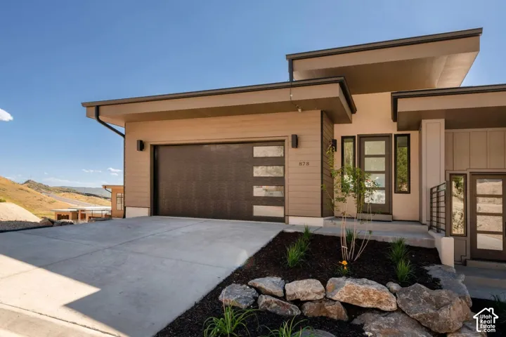 Modern architectural exterior with a flat roofline, integrated two-car garage with frosted glass panels, concrete driveway, and an entry featuring a multi-pane glass door