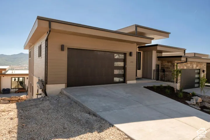 Modern architectural design with flat rooflines, stone and horizontal siding exterior, and a contemporary garage door with frosted glass panels