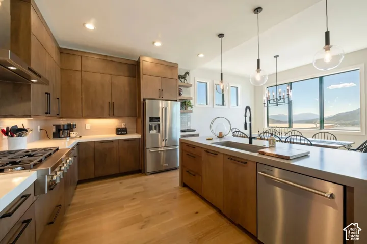 Gourmet kitchen with stainless steel appliances, wood-finish cabinetry, light-toned countertops, a large island with an integrated sink, and wood-finish flooring