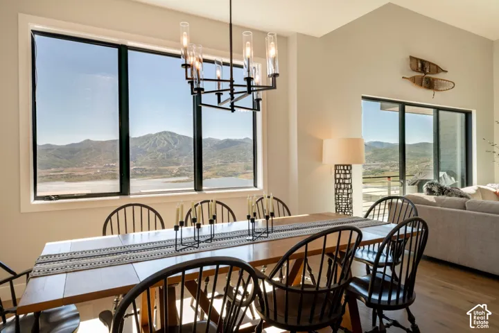 Spacious dining area featuring a prominent window framing mountain and water scenery, a contemporary chandelier, vaulted ceilings, and light wood-finish flooring