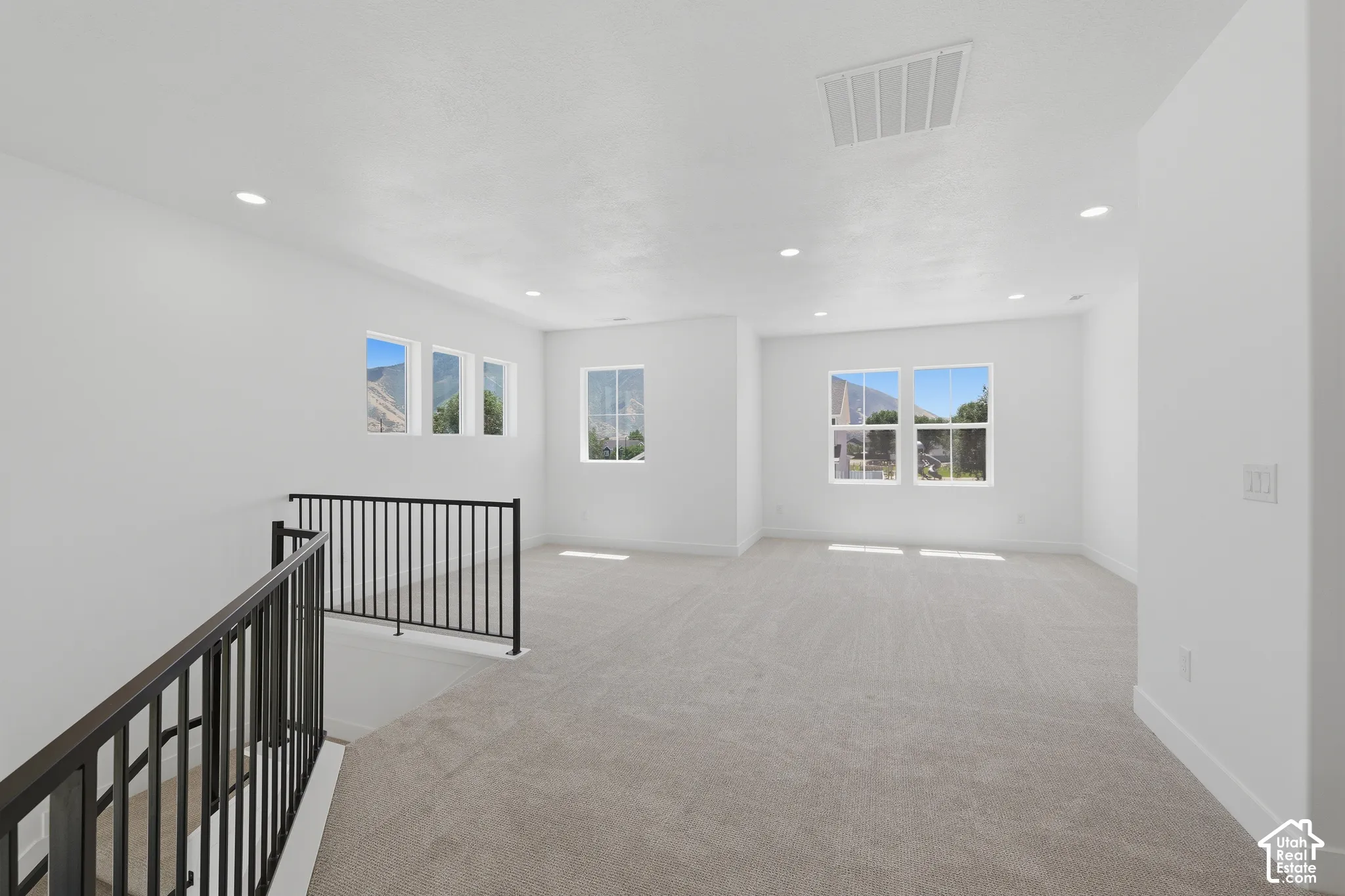 Expansive carpeted space with multiple windows, recessed lighting, and black metal railings