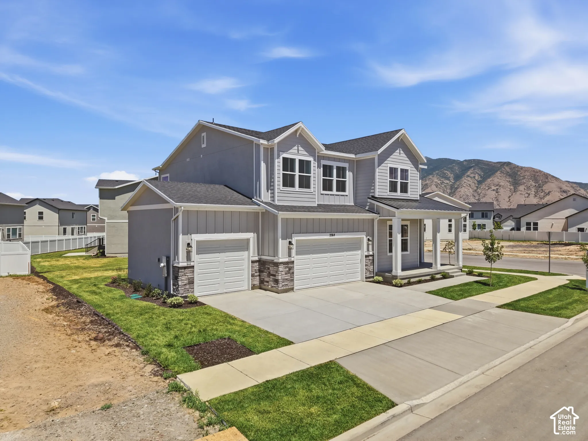 Two-story residence featuring light gray siding, stone accents, a covered front porch, and two integrated garages