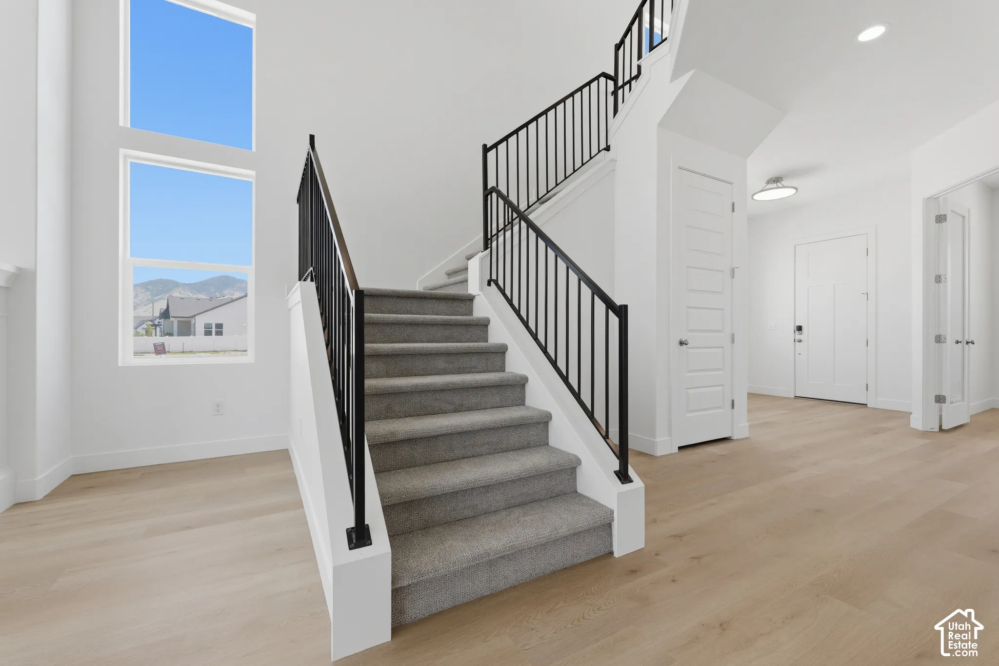 Light wood-finish flooring with a carpeted staircase and black metal railings