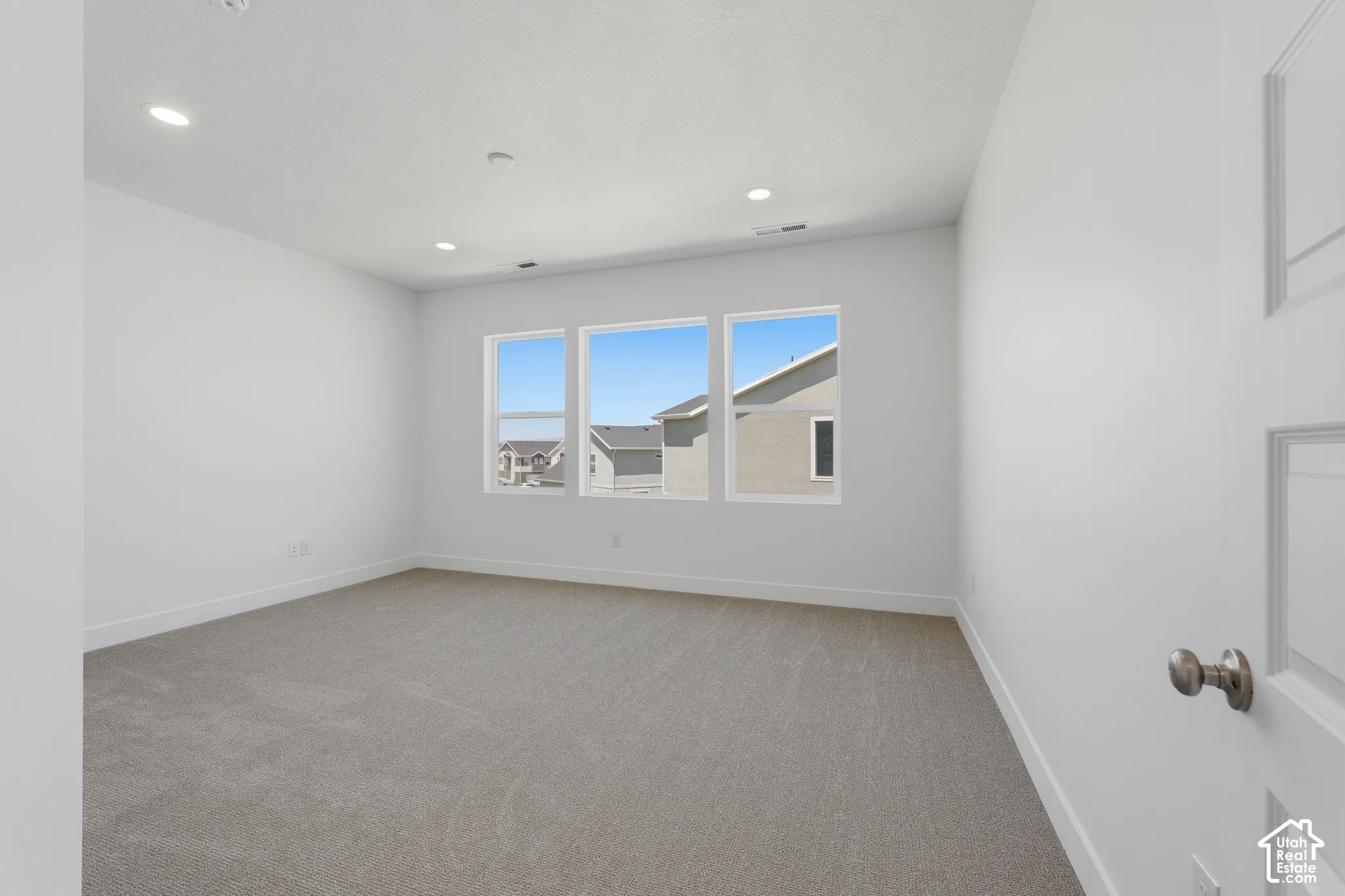Spacious room featuring neutral carpeting, white painted walls, three large windows, and recessed lighting