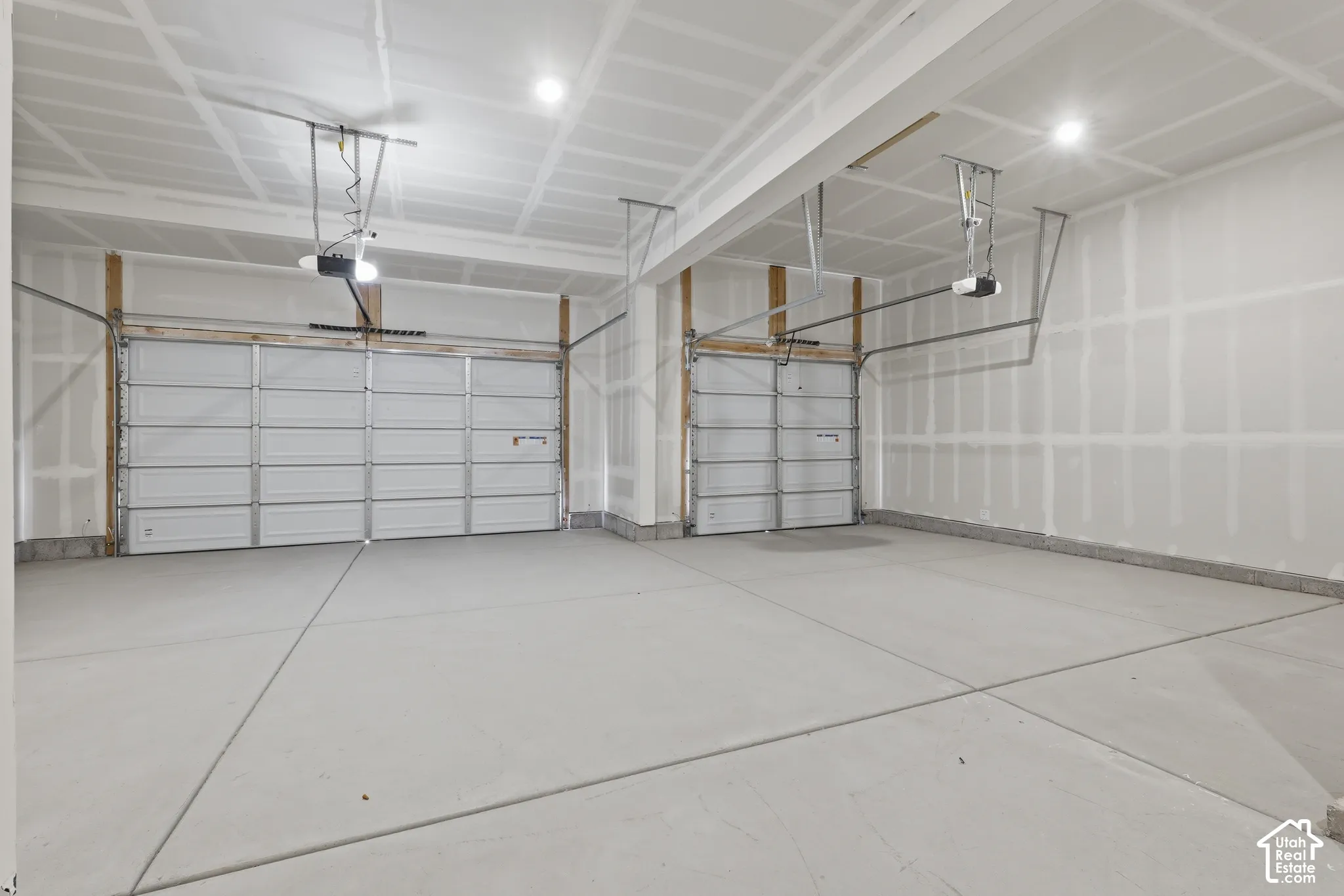 Two vehicle bays with automatic garage door openers and concrete flooring