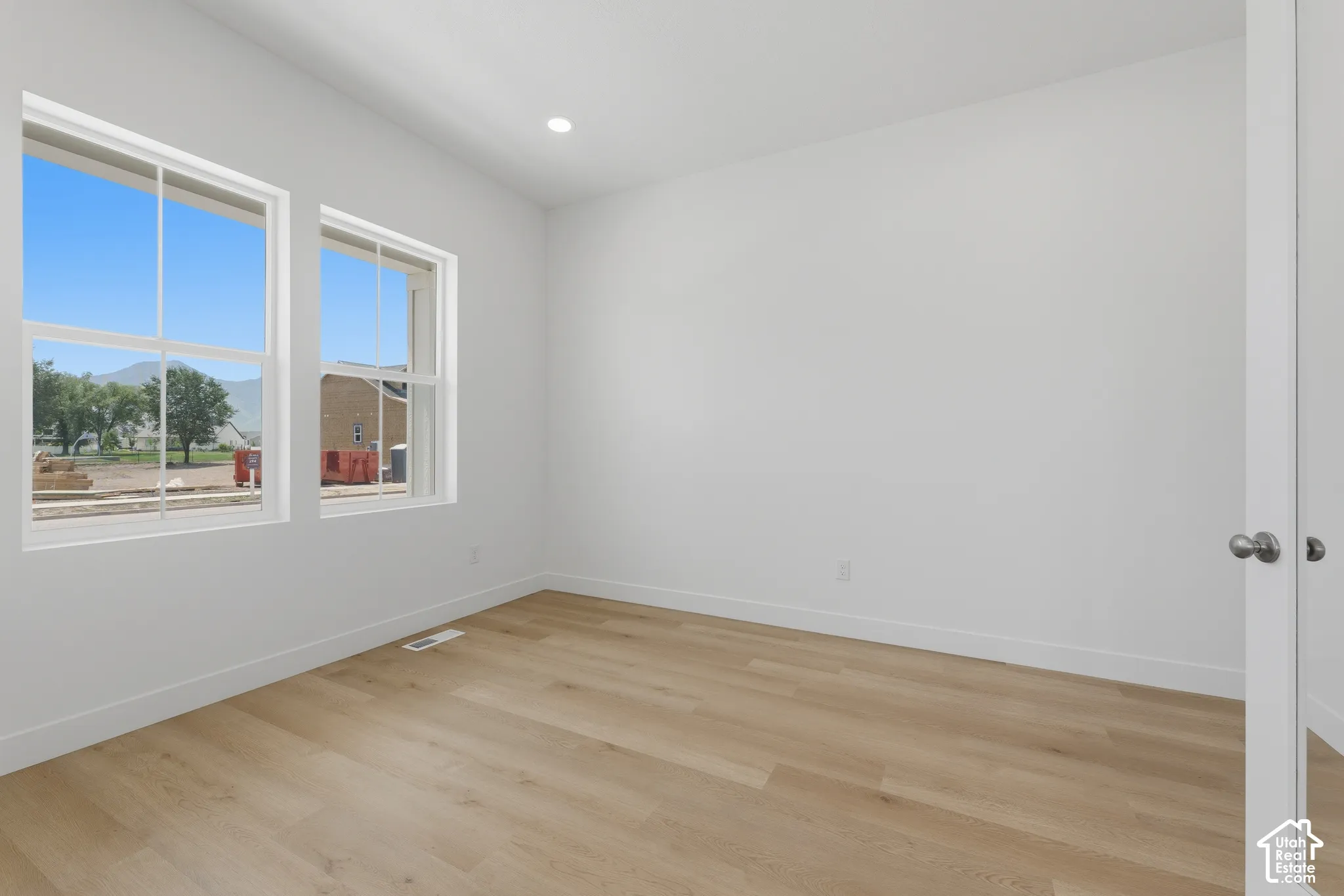 Recessed lighting illuminates the space, featuring two large windows, wood-finish flooring, and white trim