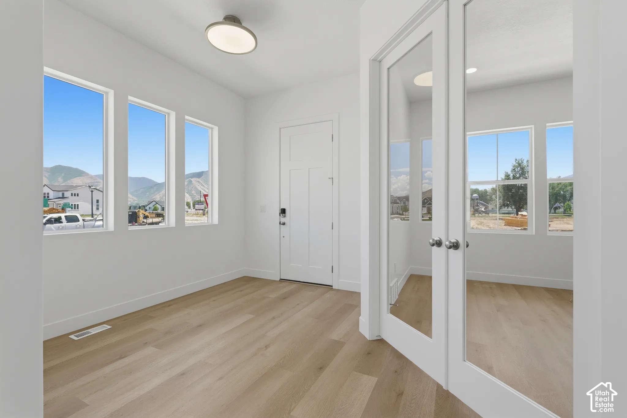 Wood-finish flooring, white trim throughout, triple window array, flush-mount ceiling light, and glass-paneled double doors