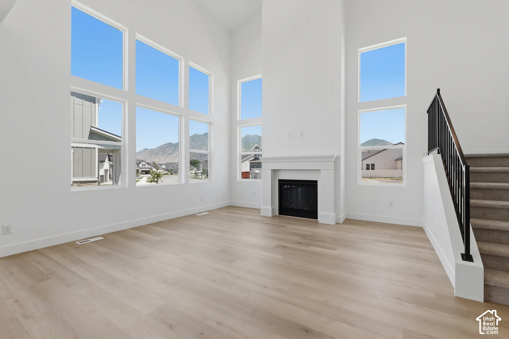 Two-story living area featuring a fireplace with a white mantel, large multi-pane windows, wood-finish flooring, and a staircase with a black metal railing
