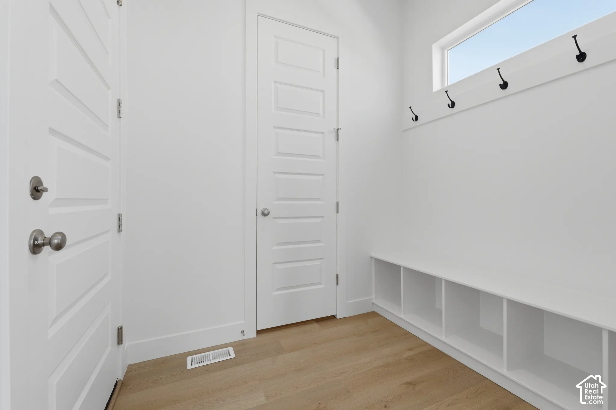Wood-finish flooring, built-in storage bench with cubbies, upper wall-mounted hooks, transom window, and white paneled doors