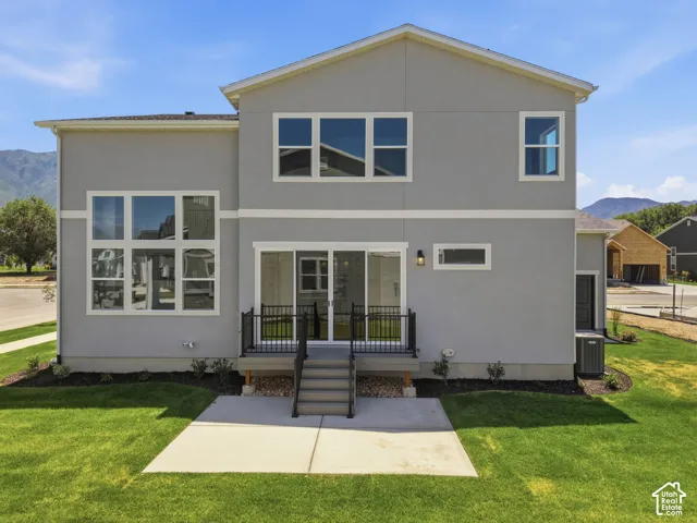 Contemporary stucco exterior with multiple large pane windows, a ground-level concrete patio, a raised deck with dark railing, and a sliding glass door entry
