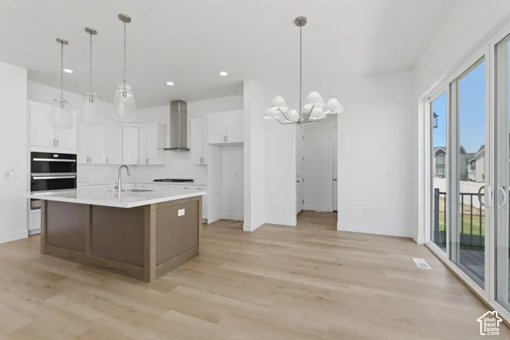 Open-concept kitchen and dining area featuring white cabinetry, a center island with a sink, double wall ovens, and wood-finish flooring