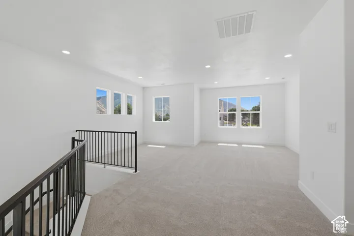 Expansive carpeted space with multiple windows, recessed lighting, and black metal railings
