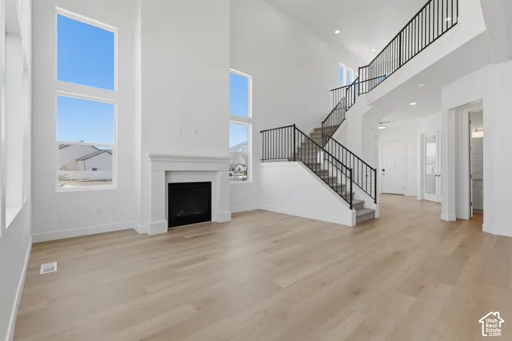 Two-story living area featuring a fireplace with a white mantel, multiple tall windows, and light wood-finish flooring