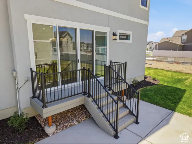 Exterior deck with composite decking and black metal railings, featuring sliding glass doors and concrete steps leading to a manicured lawn