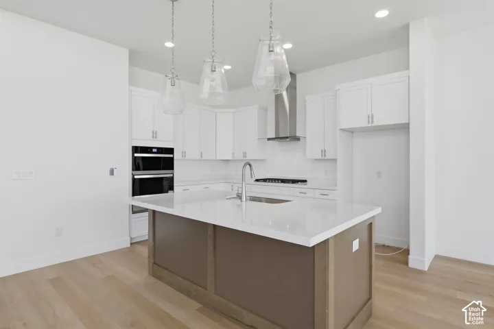 Open-concept kitchen featuring an expansive island with a light-toned countertop, white cabinetry, integrated stainless steel double ovens, a stainless steel range hood, and wood-finish flooring