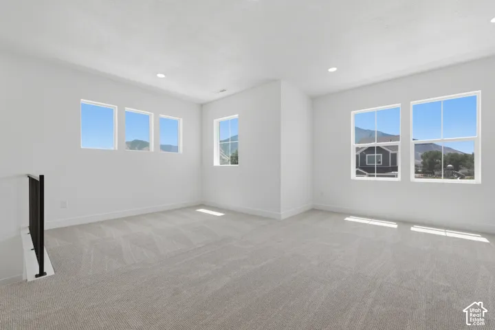 Recessed lighting illuminates an open space featuring light gray carpeting, crisp white walls, and multiple windows